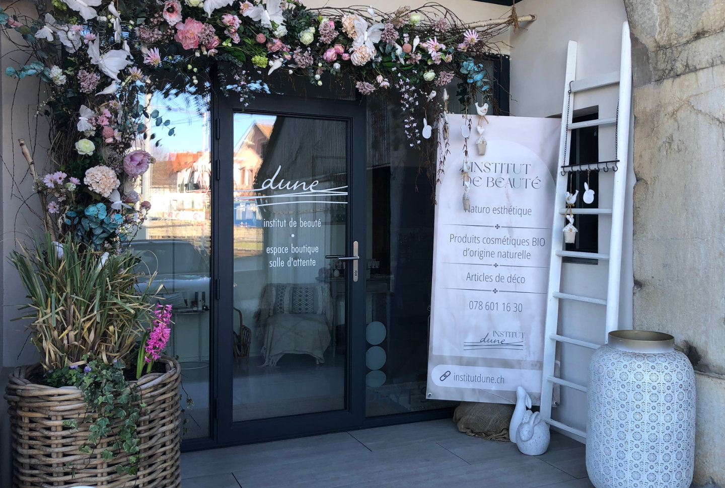 Entrée de l'institut Dune" ornée d'un arc floral rose et blanc, avec une bannière listant les services proposés.