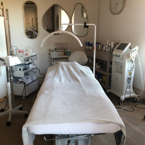 Salle de soin lumineuse avec table de massage blanche, miroirs dorés et équipements esthétiques professionnels.